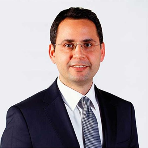 A businessman in a dark suit and tie poses against a plain background, exuding professionalism.