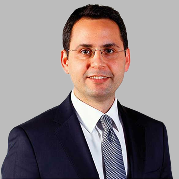 Düz bir arka planda poz veren, koyu takım elbise ve kravat giymiş bir işadamı profesyonellik yayıyor.